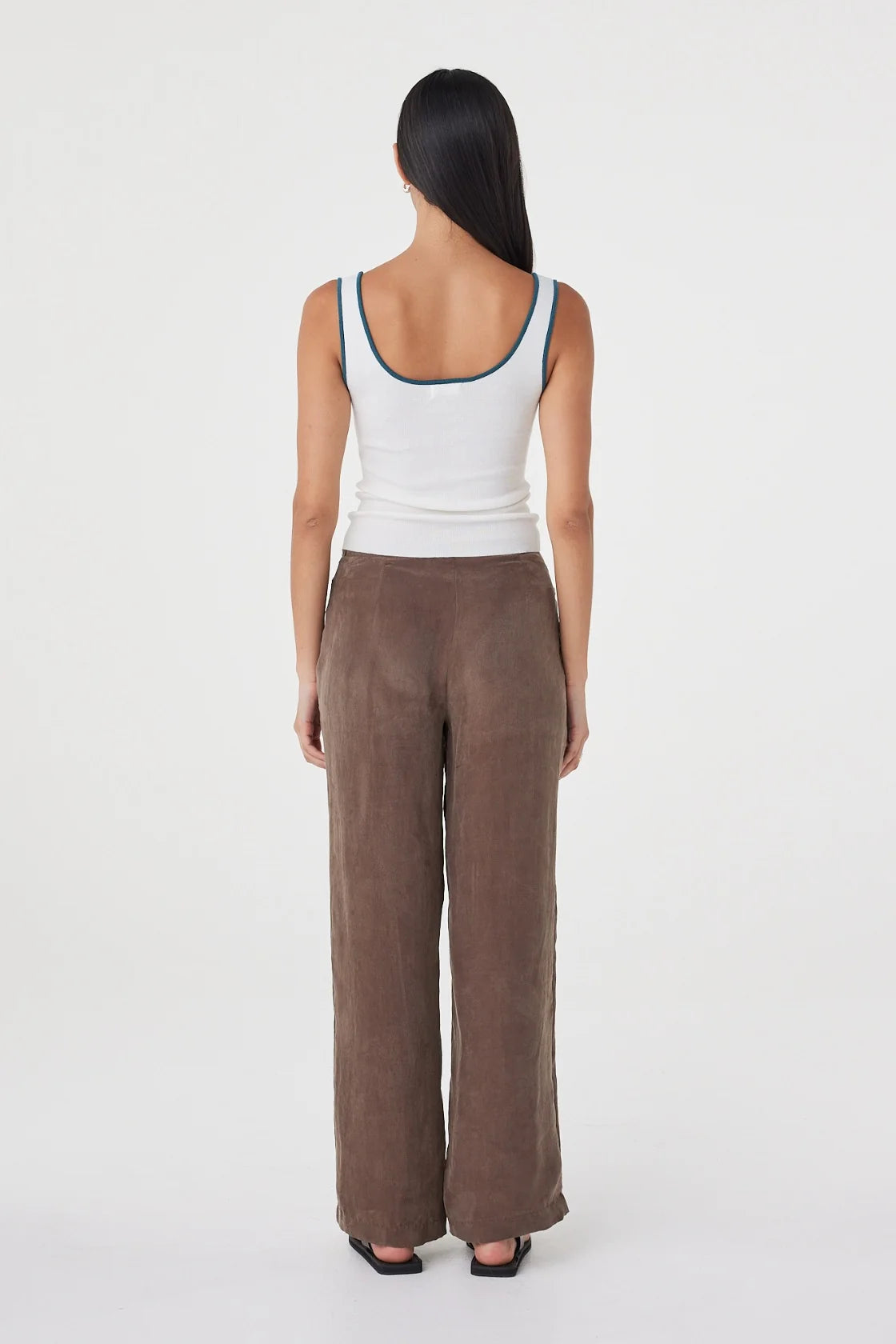 Back view of the cream fitted tank with teal contrast trim at the neckline and straps, styled with brown wide-leg wrap pants and black sandals against a clean white studio background.