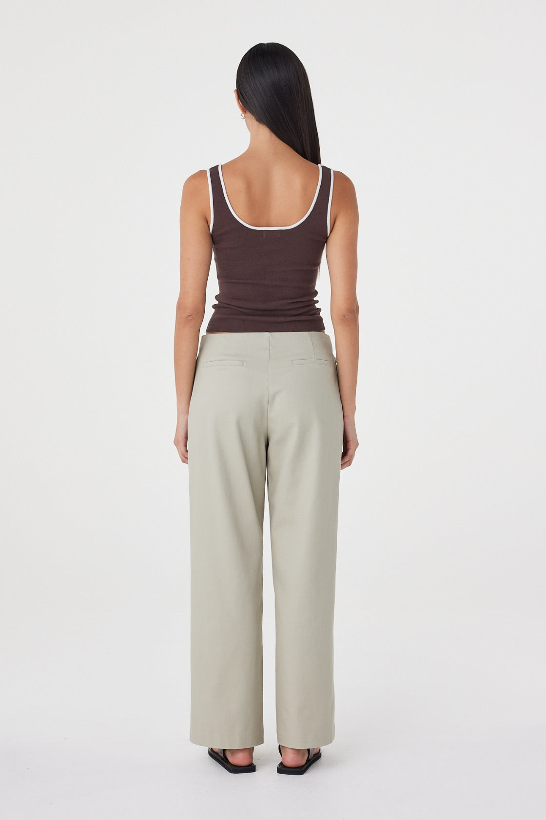 Model wearing the espresso fitted tank with cream tailored trousers, showing the square scoop back, wide shoulder straps, contrast cream edging and close-to-body silhouette in a full-length back view.