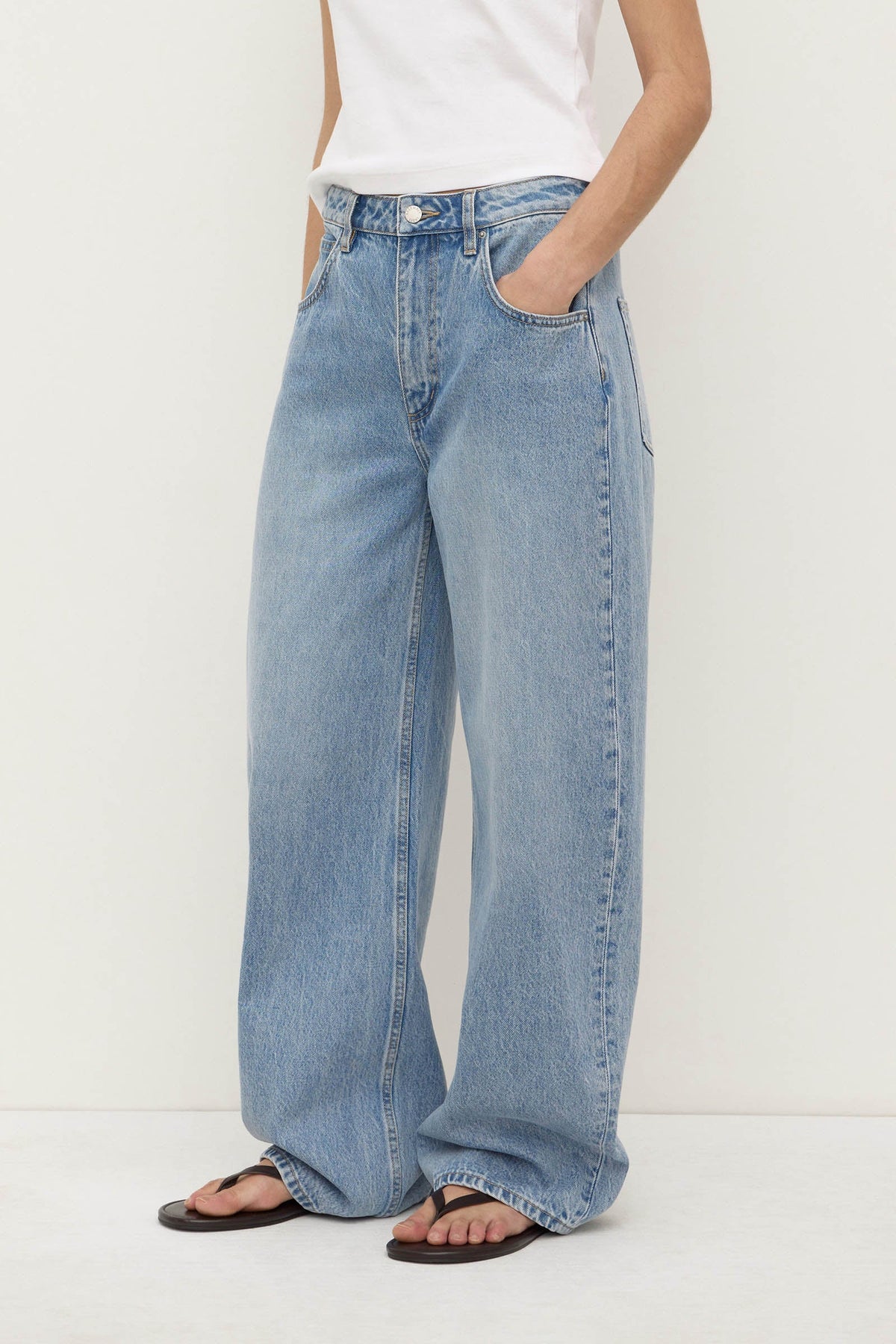 Side-front view of indigo fade relaxed jeans showing the mid-rise waist, curved outer seam and wide leg extending to the hem.