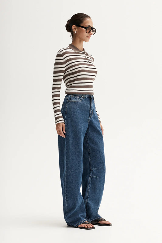 Model wearing a brown and white striped long-sleeve polo top with blue wide-leg jeans and black glasses, showing the straight silhouette and side profile