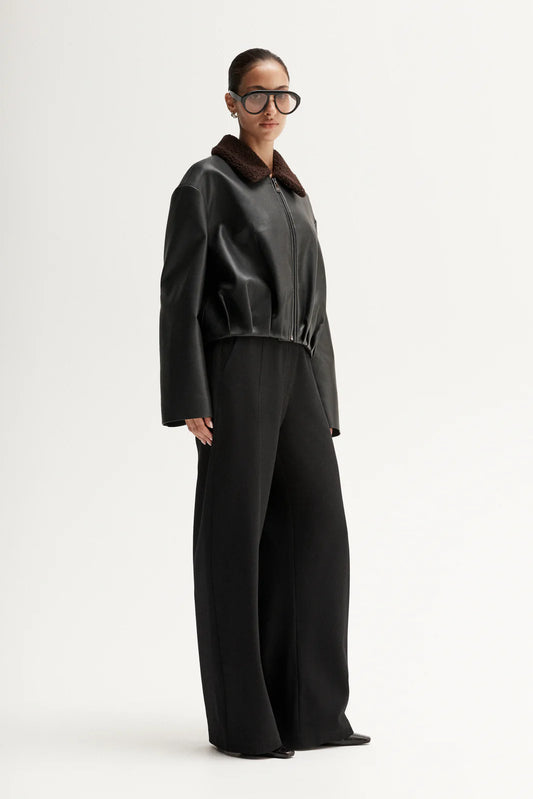 Person wearing a dark gray jacket and wide-leg pants on a white background