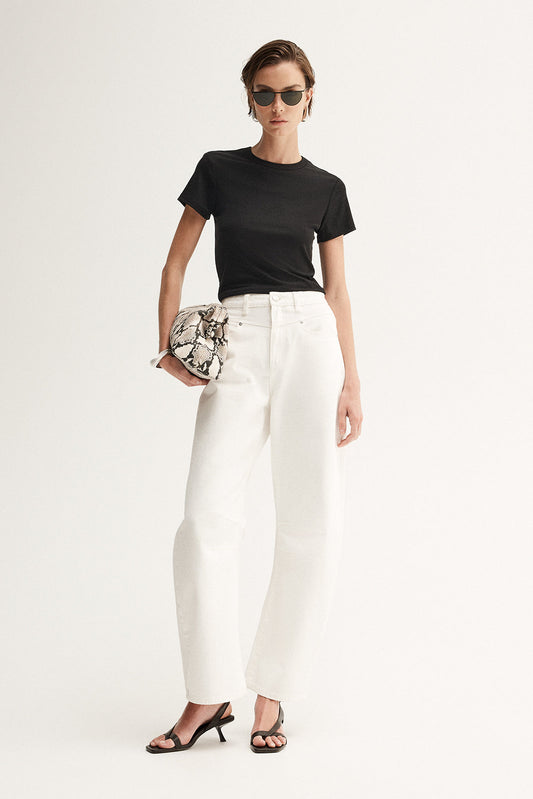 A model wearing a fitted black crew-neck tee and white wide-leg trousers, accessorised with dark sunglasses, a patterned clutch and black heeled sandals in a front-facing studio pose.