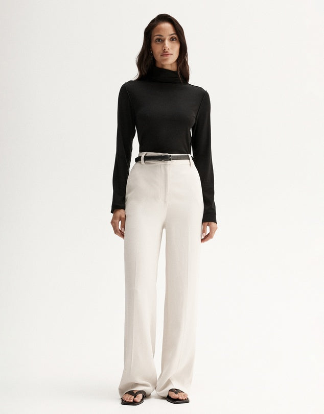 Model wearing a black fitted long-sleeve top with white wide-leg trousers and black sandals, full-length front view