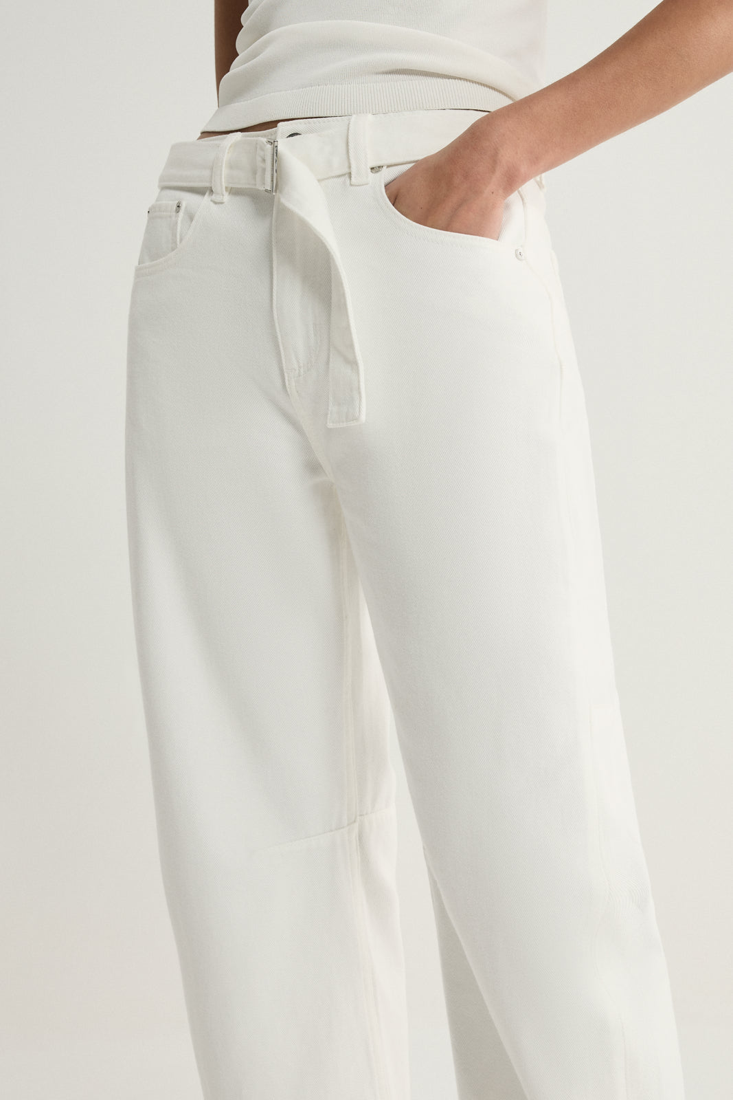 A detailed view of ivory wide-leg denim pants showing the waist tie threaded through a belt loop, front pocket opening, waistband stitching and the denim surface.
