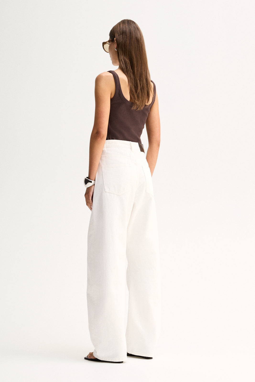 Back view of a woman wearing a chocolate tank with wide shoulder straps, paired with white wide-leg pants.