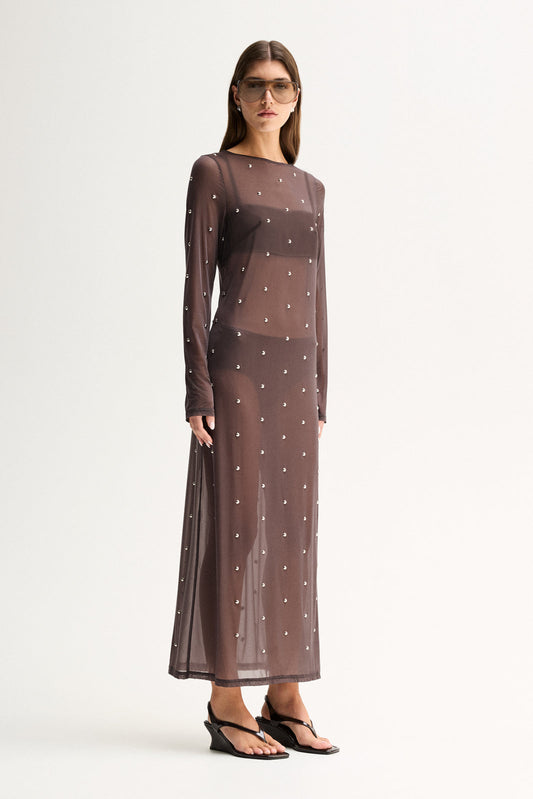 Three-quarter front view of a woman wearing a slate sheer maxi dress with long sleeves and all-over stud detailing.