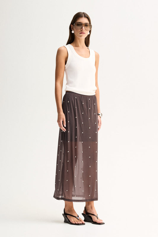 Three-quarter view of a woman wearing a slate sheer midi skirt with scattered stud details and a white sleeveless top.