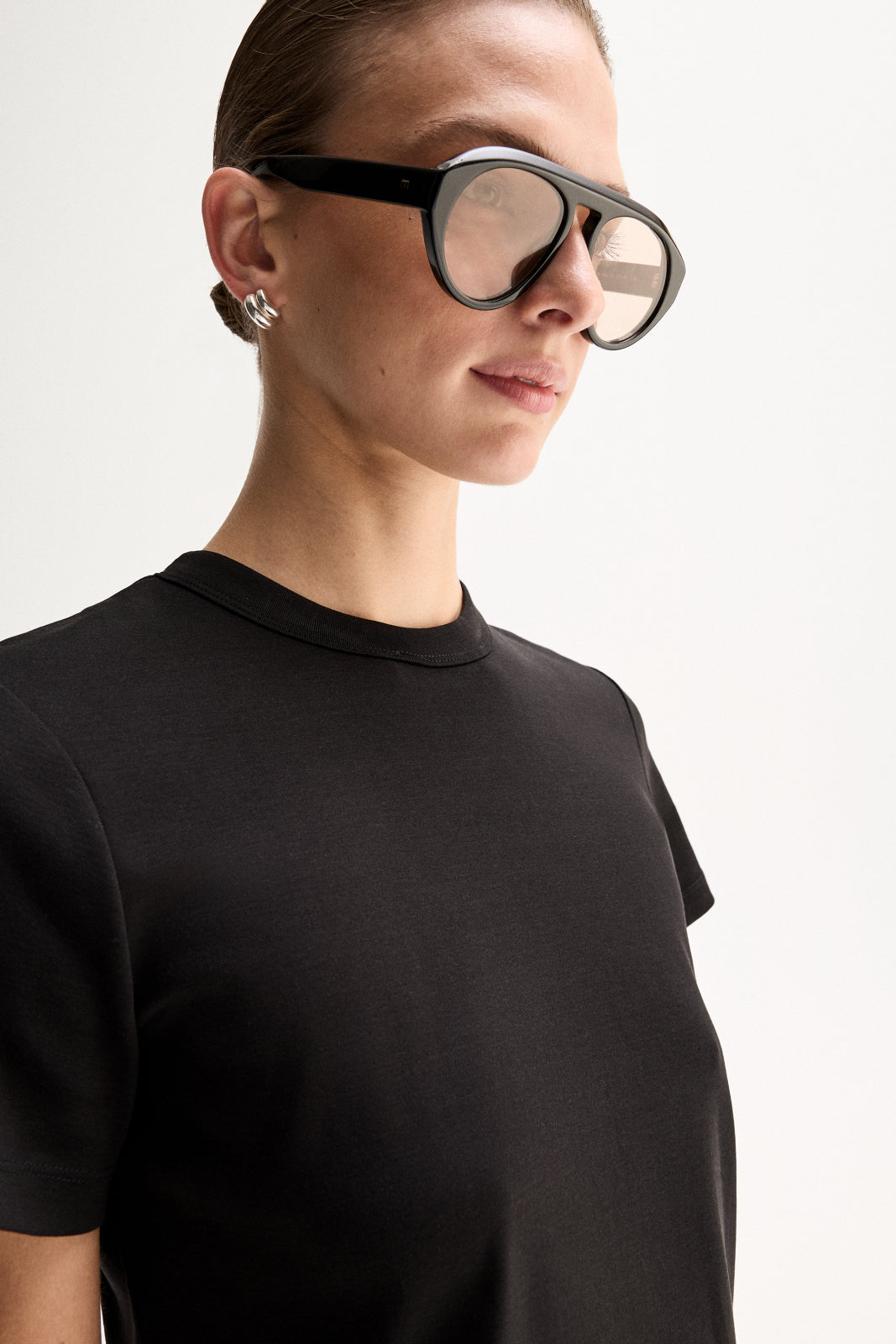 A close-up of a black T-shirt showing the round crew neckline, neatly finished collar seam and short sleeve against the upper chest.