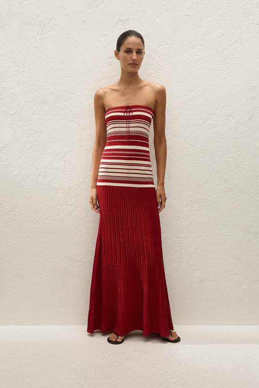 A woman wears a red and cream striped strapless maxi dress with a long pleated red skirt.