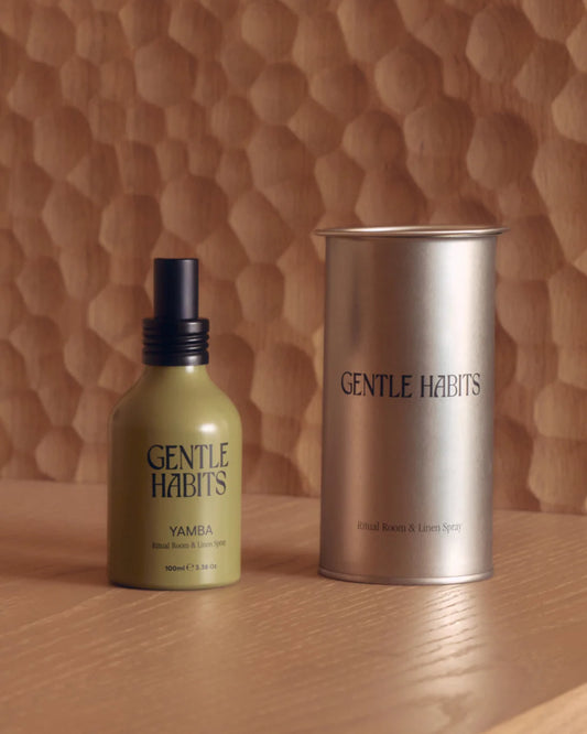Yamba room and linen spray shown on a round table beside its metal container and a dark ceramic vessel.