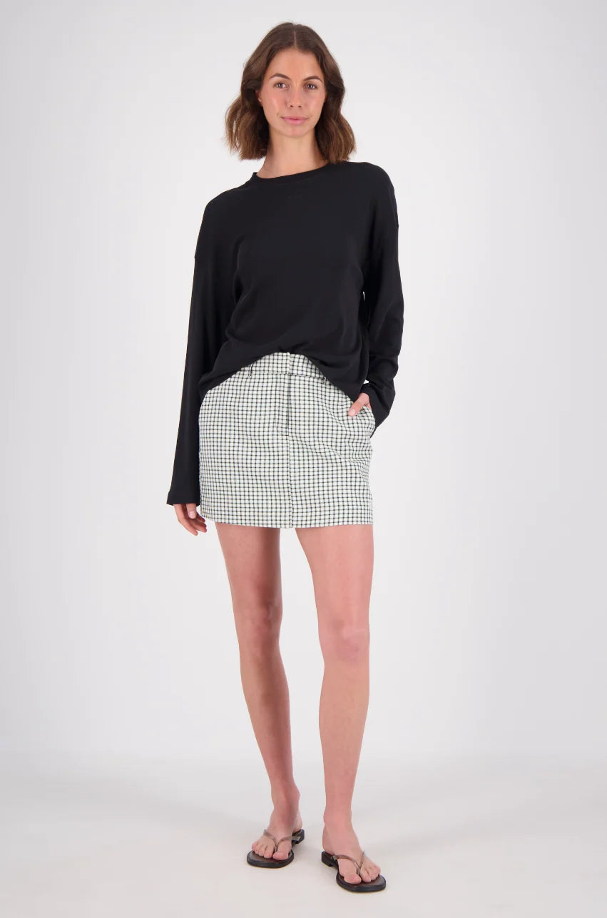 A woman wearing a white and mint checked mini skort with a black long-sleeve top, photographed from the front in a studio setting.