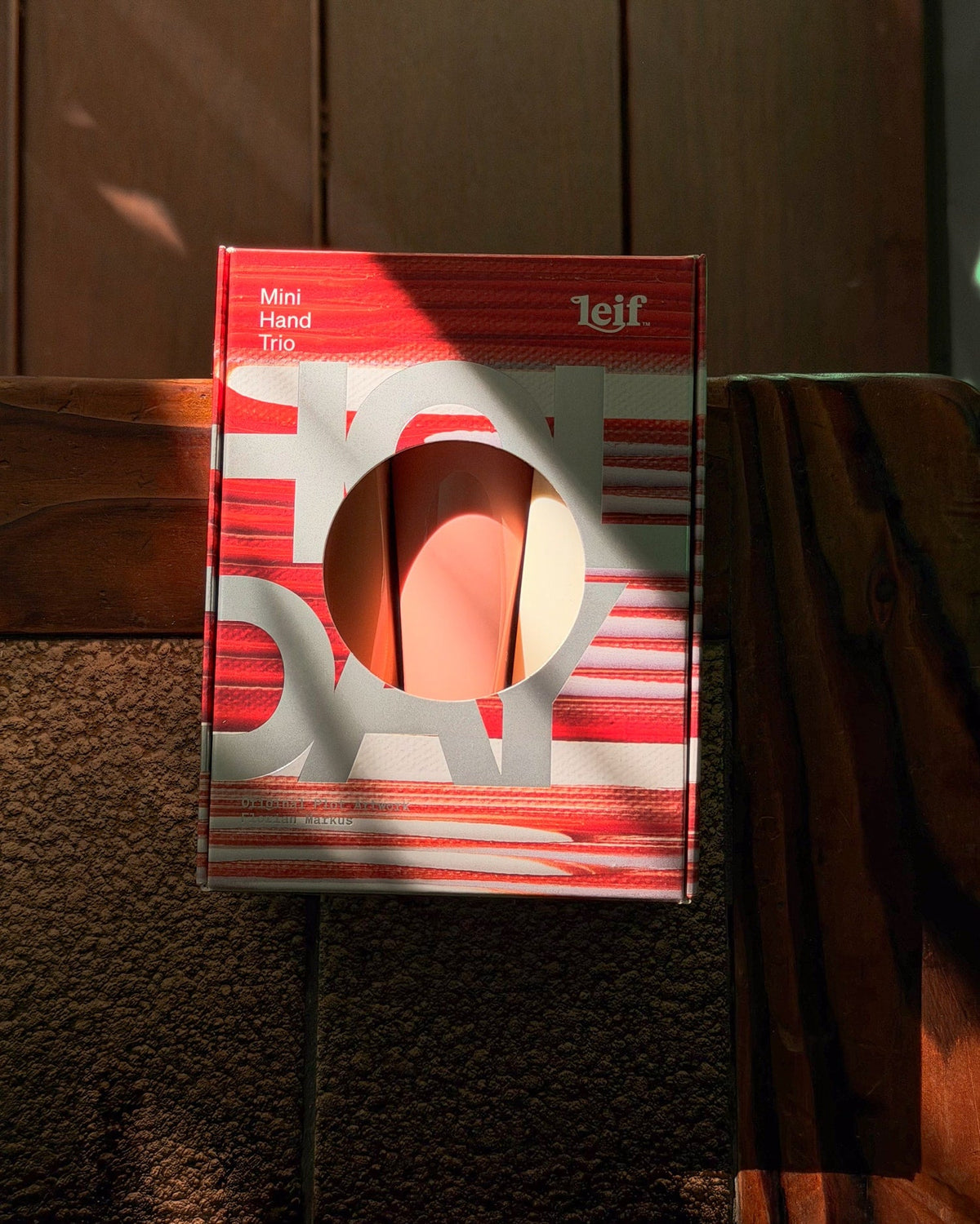 A red and white striped gift box with a circular cutout standing on a dark wooden surface in warm lighting.