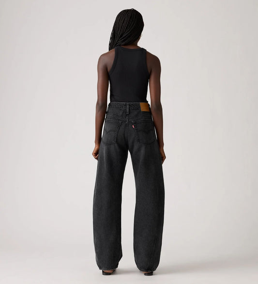 Person wearing black sleeveless top and wide-leg jeans on a plain background