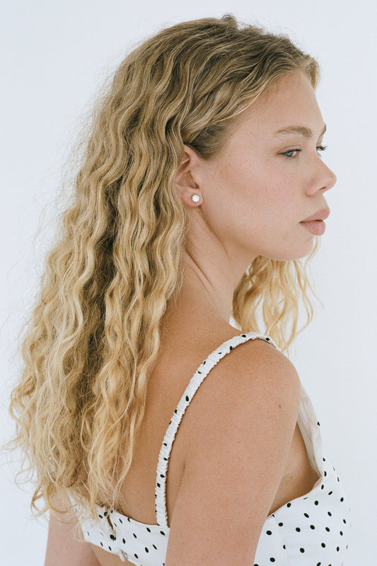 Woman with long, wavy blonde hair wearing a white polka dot dress against a white background