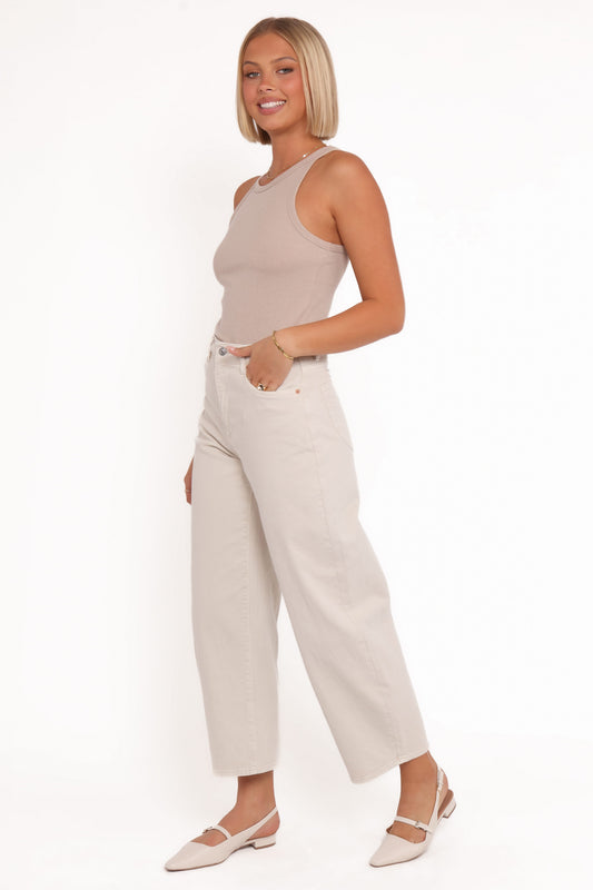 Side three-quarter view of a model wearing off-white high-rise barrel jeans with a beige sleeveless top and ballet flats, highlighting the curved leg shape and cropped hems.
