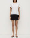 Person wearing a white t-shirt and black skirt on a plain background