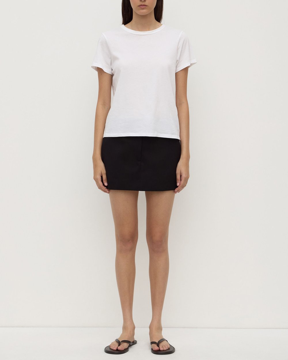 Person wearing a white t-shirt and black skirt on a plain background