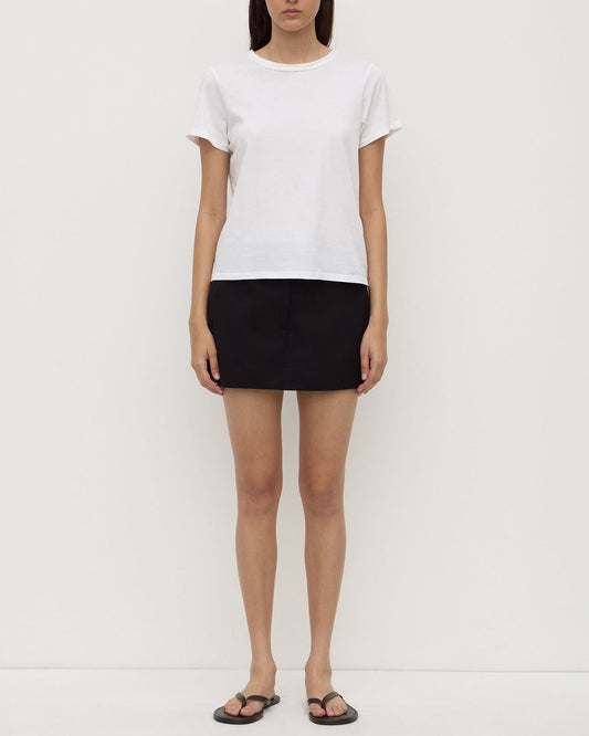 Person wearing a white t-shirt and black skirt on a plain background