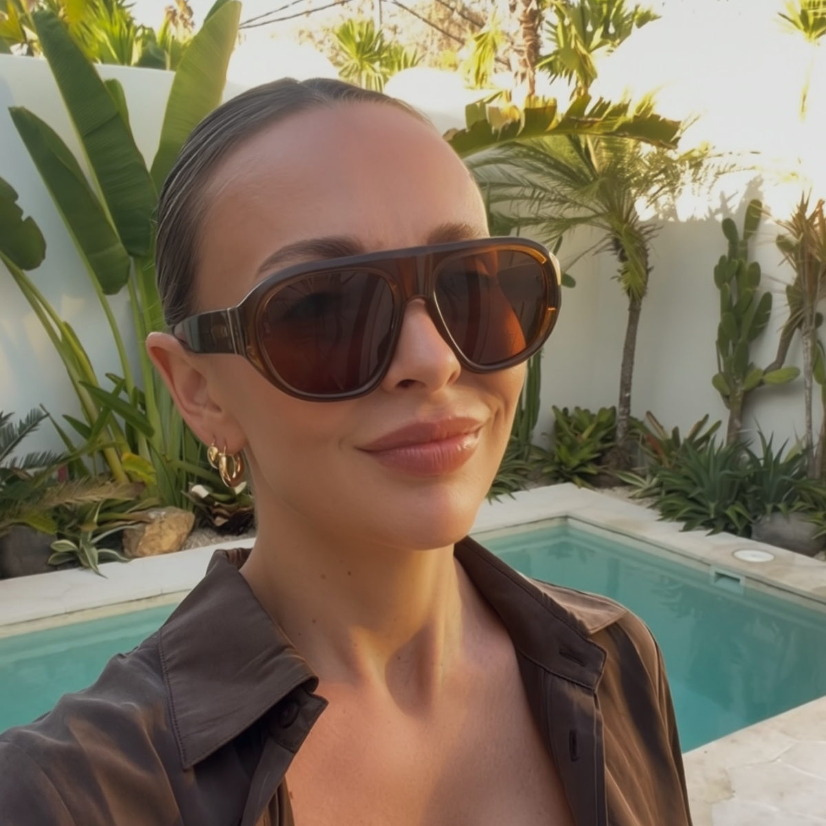 A woman wearing the Whiskey sunglasses in a close-up outdoor setting beside a swimming pool.
