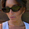 Model wearing the 180EYEWEAR 'Gia' sunglasses in gloss black with black lenses, close-up lifestyle shot against a wood-panel background.