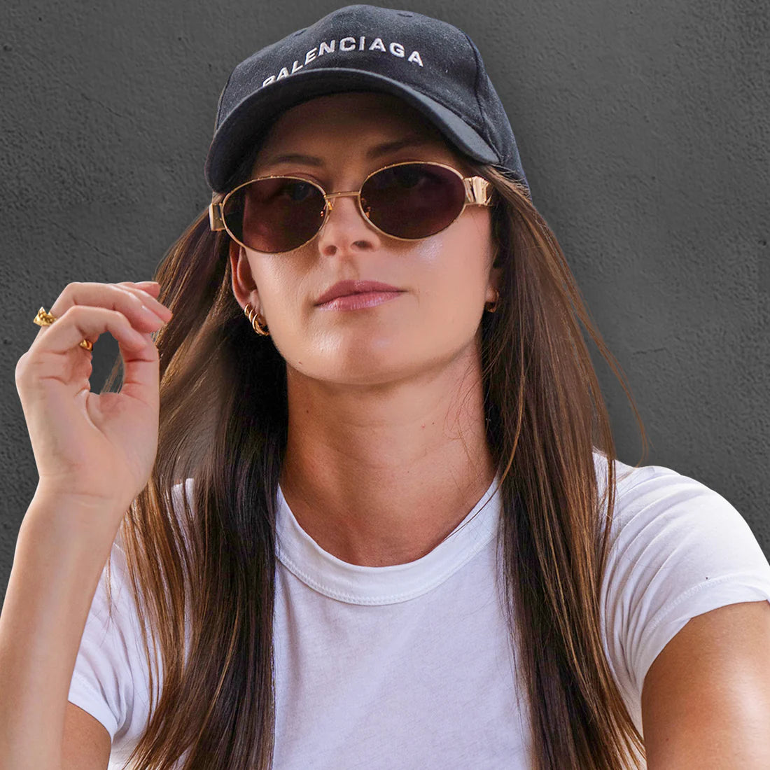 Model wearing the 180EYEWEAR 'Isla' sunglasses in gold with brown lenses and a black cap, close-up lifestyle shot against a charcoal grey background.
