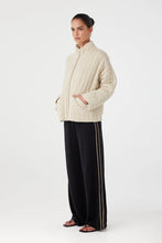 Woman wearing a cream sweater and black pants with white stripes on a white background