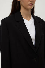 Person wearing a black blazer over a white shirt on a plain background