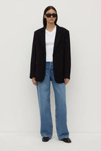 Person wearing a black blazer, white shirt, and blue jeans on a white background