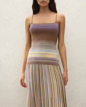 Woman wearing a two-tone dress with a purple top and multicolored striped skirt against a white background