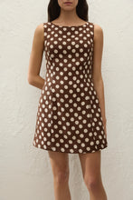 Woman wearing a brown dress with white polka dots against a plain background