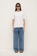 Model wearing the white tee with relaxed blue jeans, black sandals and sunglasses, showing the boxy fit, short sleeves and straight hem, full-length front view