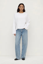 Person wearing a white top and light blue jeans on a white background