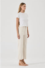 Woman wearing a white t-shirt and beige pants on a light gray background