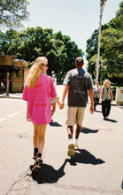 Two people walking on a street with trees and buildings in the background