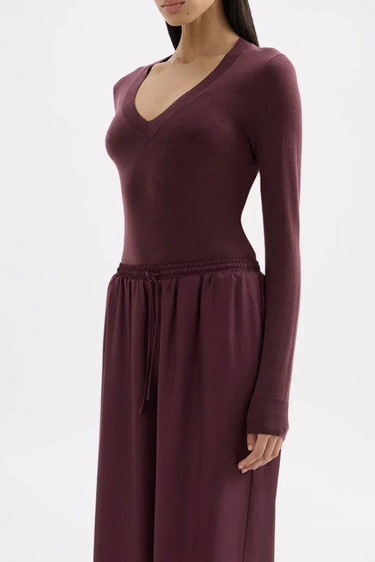 Model wearing a mulberry fitted long-sleeve V-neck knit top with matching wide-leg trousers, showing the ribbed neckline, slim silhouette and long sleeves, angled front view