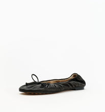 A single black leather ballet flat with gathered detailing and a small bow on the toe, shown from a side profile against a plain white background.