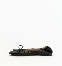 A single black leather ballet flat with gathered detailing and a small bow on the toe, shown in profile against a plain white background.