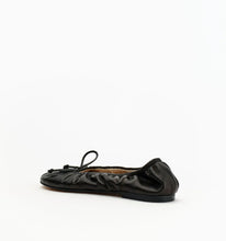 A single black leather ballet flat with a gathered, ruched upper and a small bow detail on the toe, shown from a side profile against a plain white background.