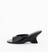 Mule in Black Oily Crinkle shown from the side with an open toe, wide leather strap and sculptural wedge heel.