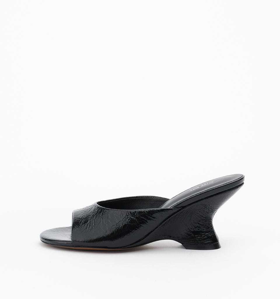 Mule in Black Oily Crinkle shown from the side with an open toe, wide leather strap and sculptural wedge heel.