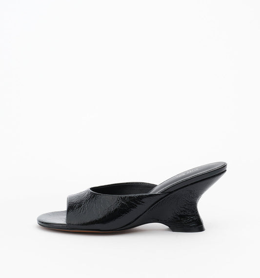 Mule in Black Oily Crinkle shown from the side with an open toe, wide leather strap and sculptural wedge heel.