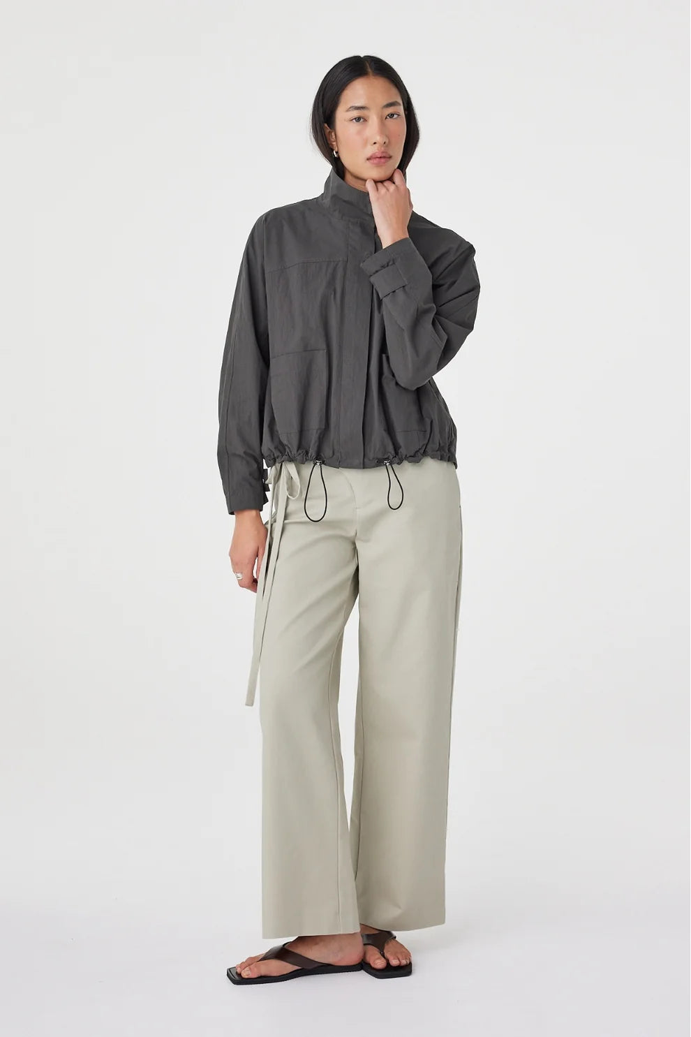 A model wears the Arcaa Addie Jacket in charcoal with light wide-leg trousers in a full-length front studio view.
