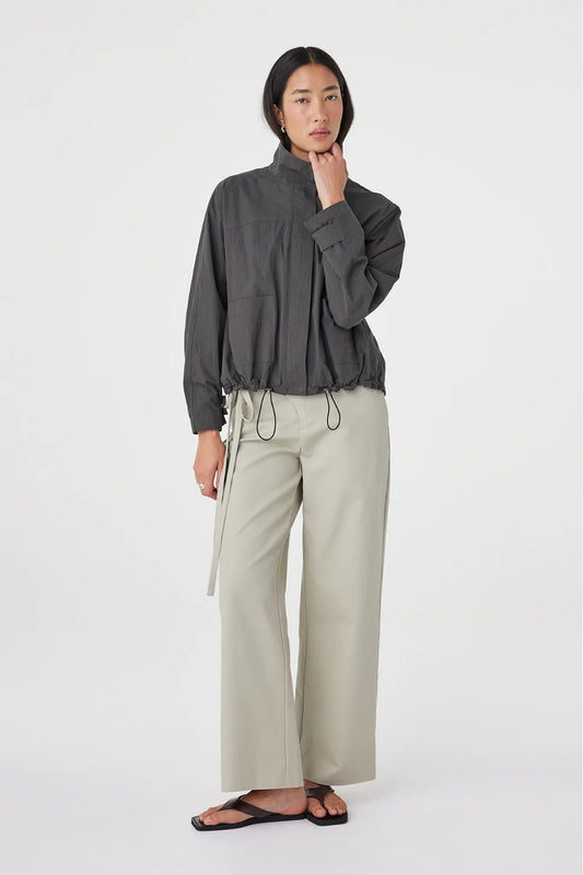 A model wears the Arcaa Addie Jacket in charcoal with light wide-leg trousers in a full-length front studio view.
