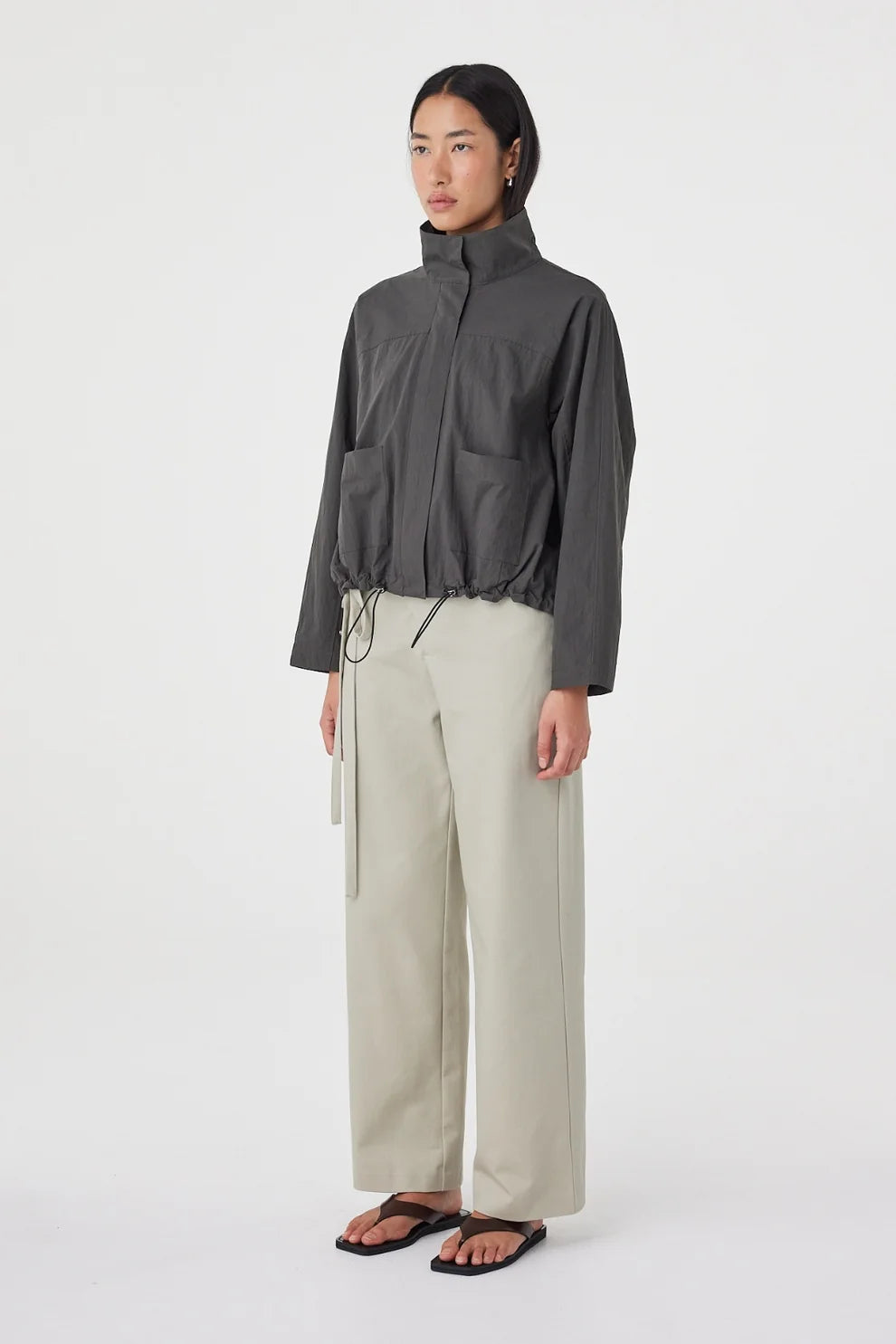 A model wears the charcoal high-neck jacket in an angled side view showing the relaxed fit and front patch pockets.
