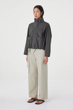 A model wears the charcoal high-neck jacket in an angled side view showing the relaxed fit and front patch pockets.
