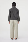 A model wears the charcoal cropped jacket in a back studio view showing the yoke seam and gathered hem.
