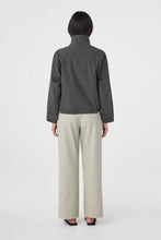 A model wears the charcoal cropped jacket in a back studio view showing the yoke seam and gathered hem.
