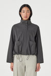 A close-up shows the high collar, concealed front fastening, patch pockets and adjustable drawcord hem on the charcoal jacket.