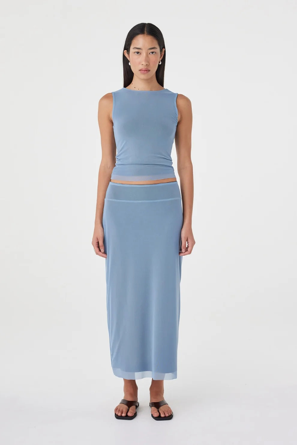 Front view of the pale blue reversible maxi skirt styled with a matching pale blue sleeveless top and black sandals against a clean white studio background.