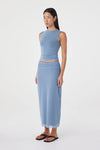 Three-quarter side view of the pale blue reversible maxi skirt styled with a matching pale blue sleeveless top and black sandals in a minimal white studio.
